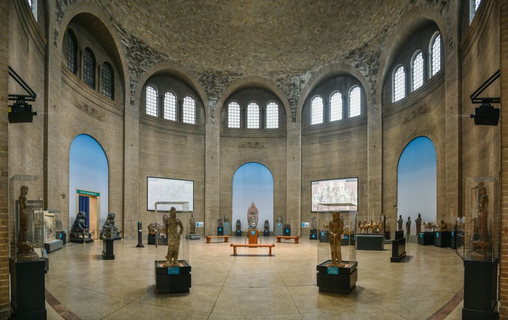 아치형 창문, 유리 케이스의 조각상, 벽면 디스플레이가 있는 넓은 박물관 홀. 객실에는 돔형 천장과 돌담이 있습니다.