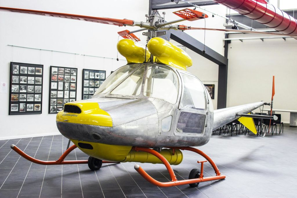 실내에는 금속 바디와 노란색으로 포인트를 준 빈티지 헬리콥터가 전시되어 있으며, 액자에 담긴 사진이 벽을 배경으로 전시되어 있습니다.