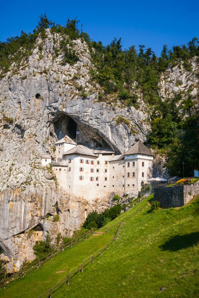 녹지와 나무로 둘러싸인 바위 절벽에 지어진 중세 성으로 이어지는 작은 돌다리가 있습니다.