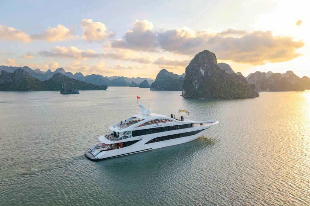 하얀 요트가 하늘 아래 바위섬으로 둘러싸인 잔잔한 바다를 항해하고 노을이 질 무렵 구름이 흩날립니다.