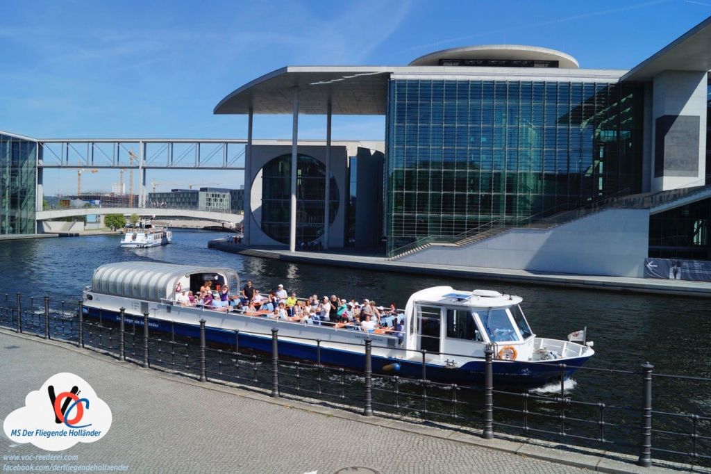 사람들로 가득 찬 투어 보트가 현대적인 유리 건물 앞을 지나고 화창한 날에는 강 위로 다리를 놓습니다.