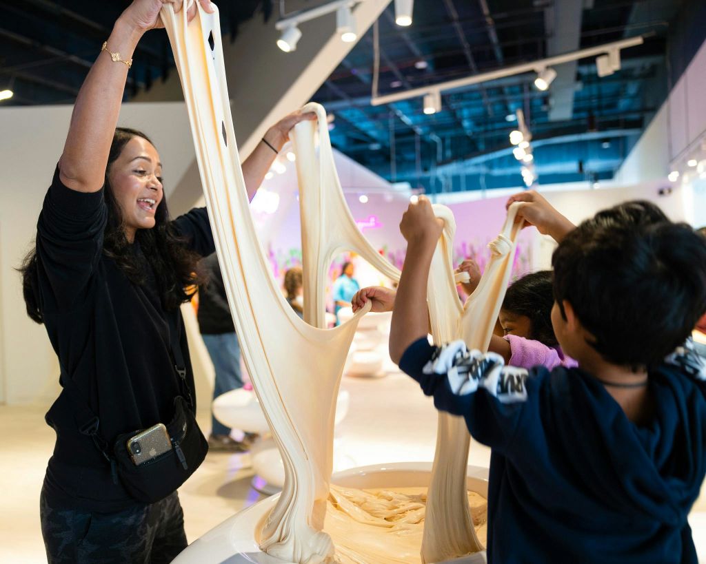 밝은 조명과 현대적인 인테리어로 꾸며진 실내 공간에서 커다란 반죽 같은 재료를 펴고 있는 사람들.