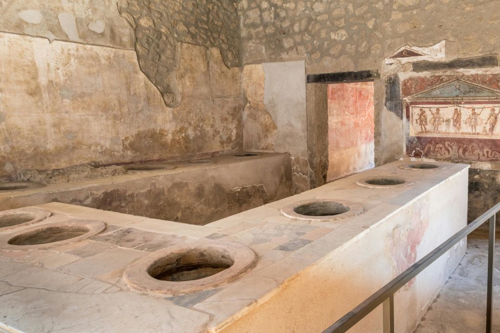 조리대에 여러 개의 원형 구멍, 돌 벽, 벽화 또는 페인트 석고 잔재가 있는 고대 석조 주방.