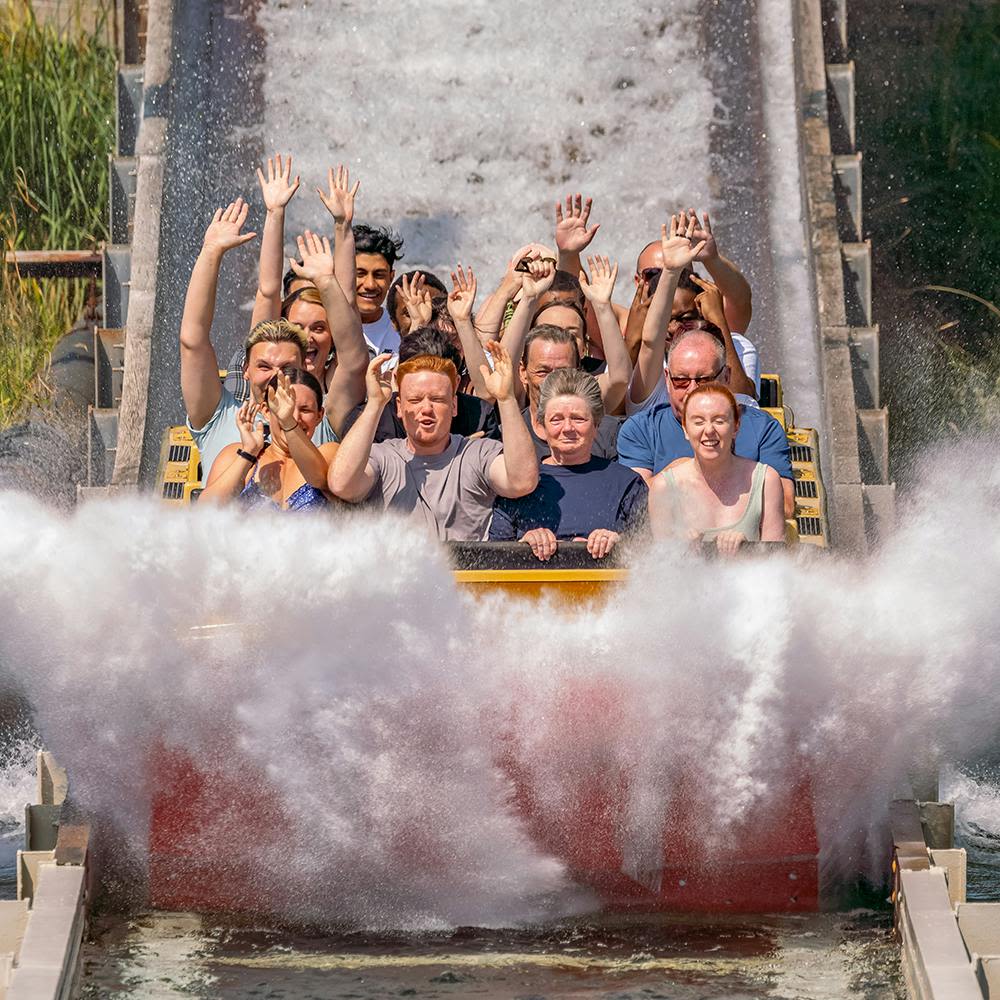 통나무에 올라타는 사람들은 주위에 물이 튀면서 손을 들고 양쪽에 파도를 일으킵니다.