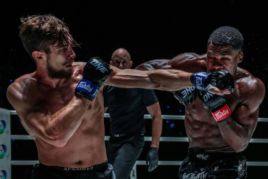 주심과 어두운 조명을 배경으로 한 복싱 링의 셔츠 없는 복서 미드 펀치.