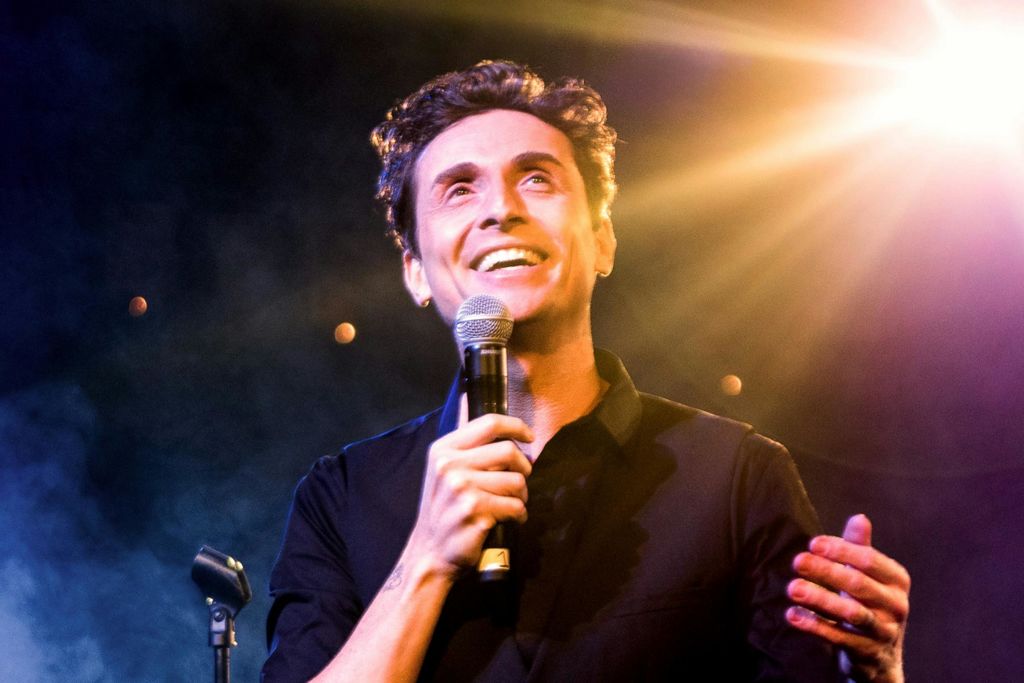 무대에서 밝은 조명으로 조명을 받고 배경이 흐릿한 상태에서 마이크를 들고 있는 사람.