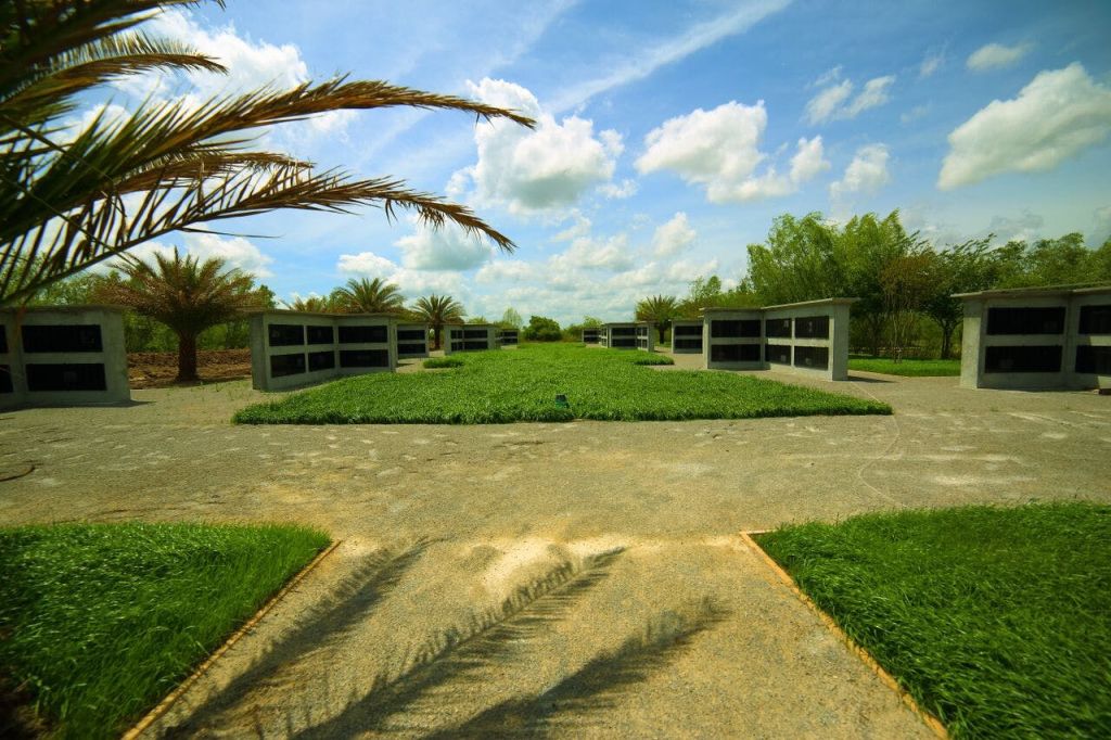 석조 묘, 푸른 잔디, 야자수, 구름이 흩날리는 푸른 하늘이 있는 조경된 공동묘지.