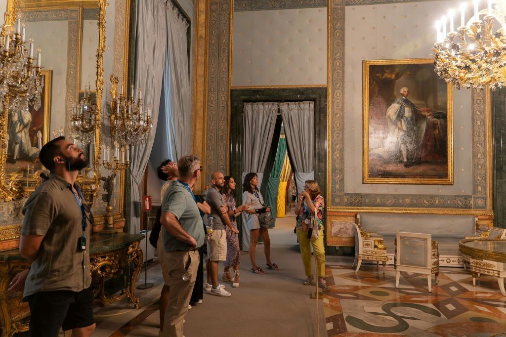 샹들리에, 예술품, 우아한 장식품이 있는 화려한 객실의 방문객들은 투어 가이드를 세심하게 관찰합니다.