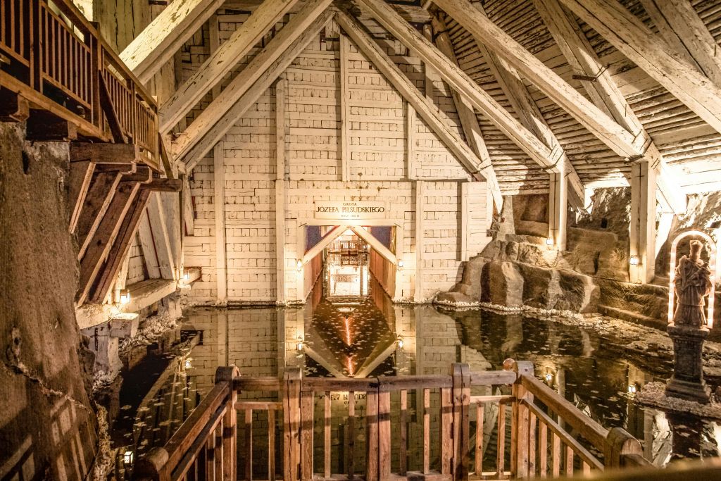 나무 기둥이 있는 석조 벽으로 된 방, "KOZiA MIEDZINSKiEGO" 라고 표시된 출입구, 벽을 반사하는 정수 수영장이 있습니다.