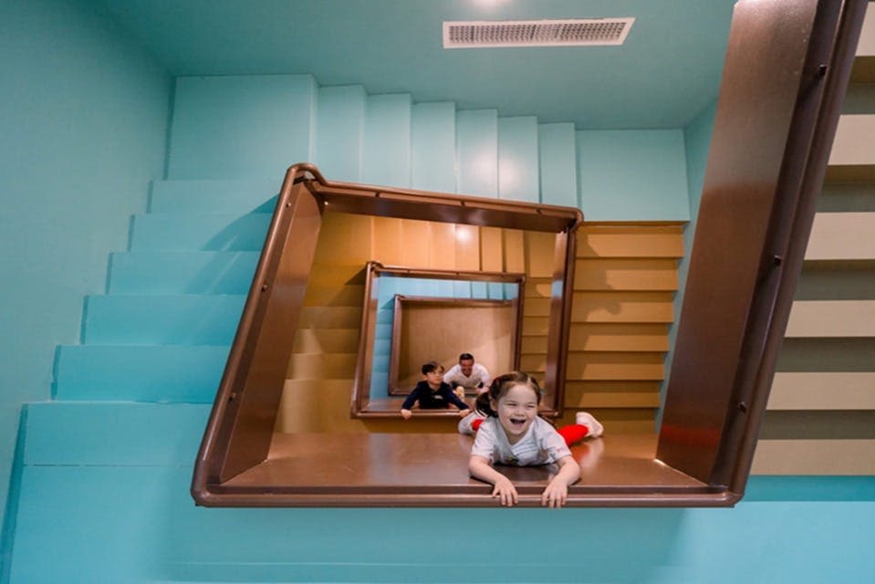 아이들이 계단을 닮은 미끄럼틀에서 놀고 있는데, 한 아이가 전방에서 미소를 짓고 있습니다.