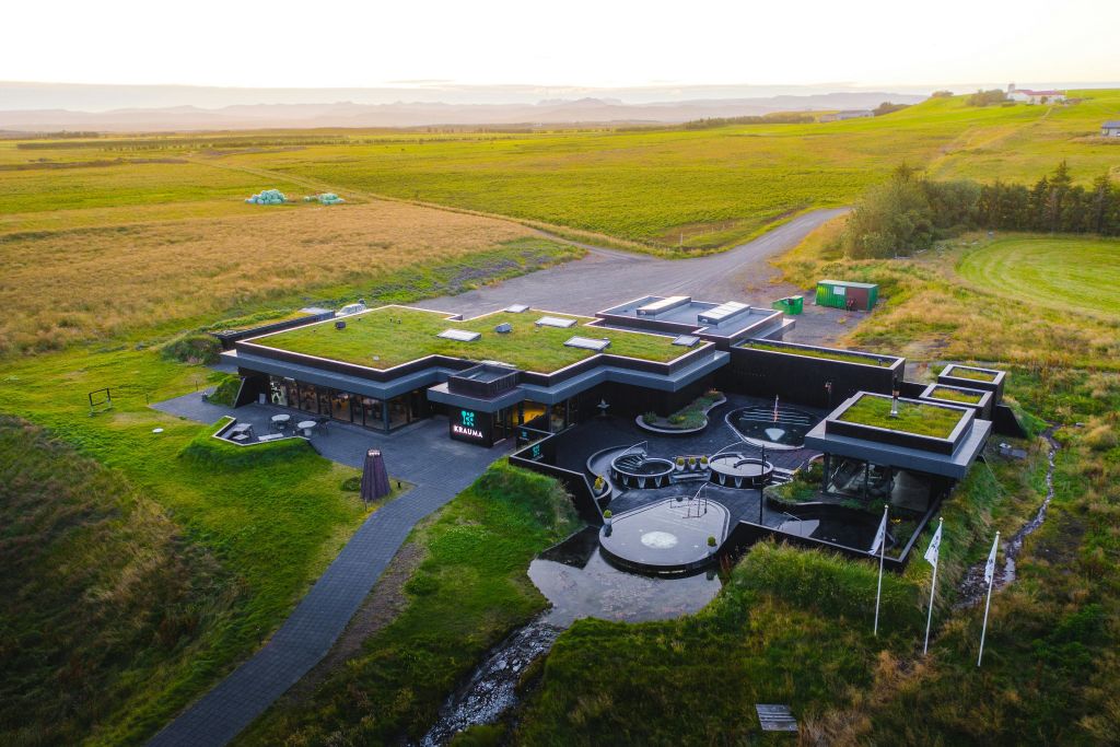 통로가 있는 잔디밭에 잔디 지붕이 있고 앞에 원형 좌석 공간이 있는 현대적인 건물입니다.