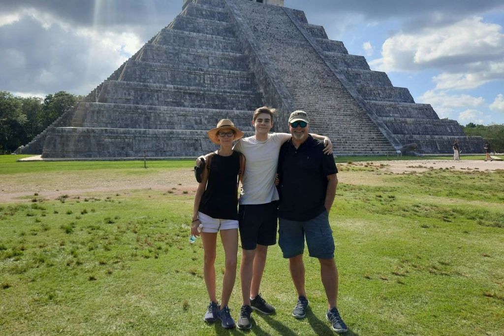 화창한 날, 커다란 석조 피라미드 앞에 세 사람이 미소를 지으며 서 있습니다.