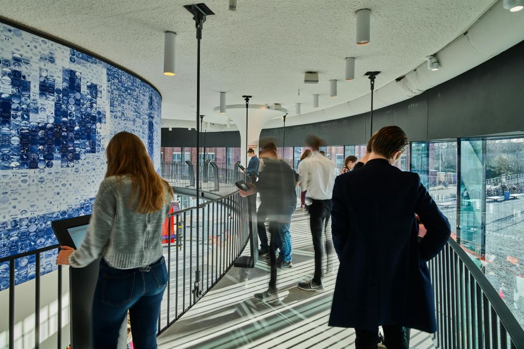 현대적인 인테리어와 조명 기구로 둘러싸인 난간이 있는 곡선형 실내 발코니에서 사람들이 걷고 서 있습니다.