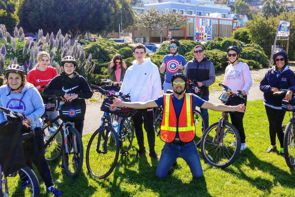 자전거를 탄 일행, 헬멧을 쓴 일행, 네온 안전 조끼를 입은 일행이 보라색 꽃 옆 야외에서 포즈를 취하고 있습니다.