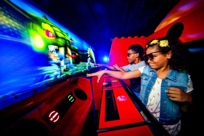 어두운 방에서 3D 안경을 쓴 두 어린이가 밝고 화려한 아케이드 게임과 상호 작용합니다.