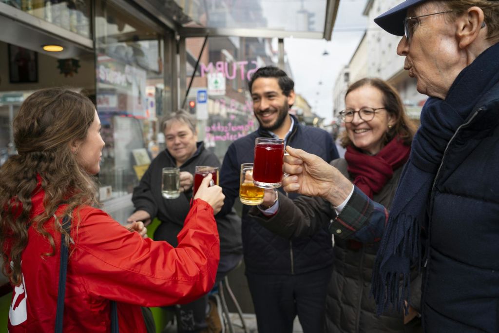 한 무리의 사람들이 야외에서 미소를 짓고 뜨거운 음료 잔을 들고 경쾌한 분위기에서 건배하는 모습을 보입니다.