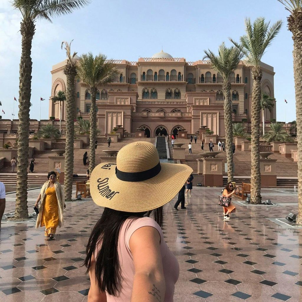 타일로 마감된 안뜰의 야자수로 둘러싸인 웅장한 건물을 바라보며 챙이 넓은 모자를 쓴 여성 걸어다니는 사람들.