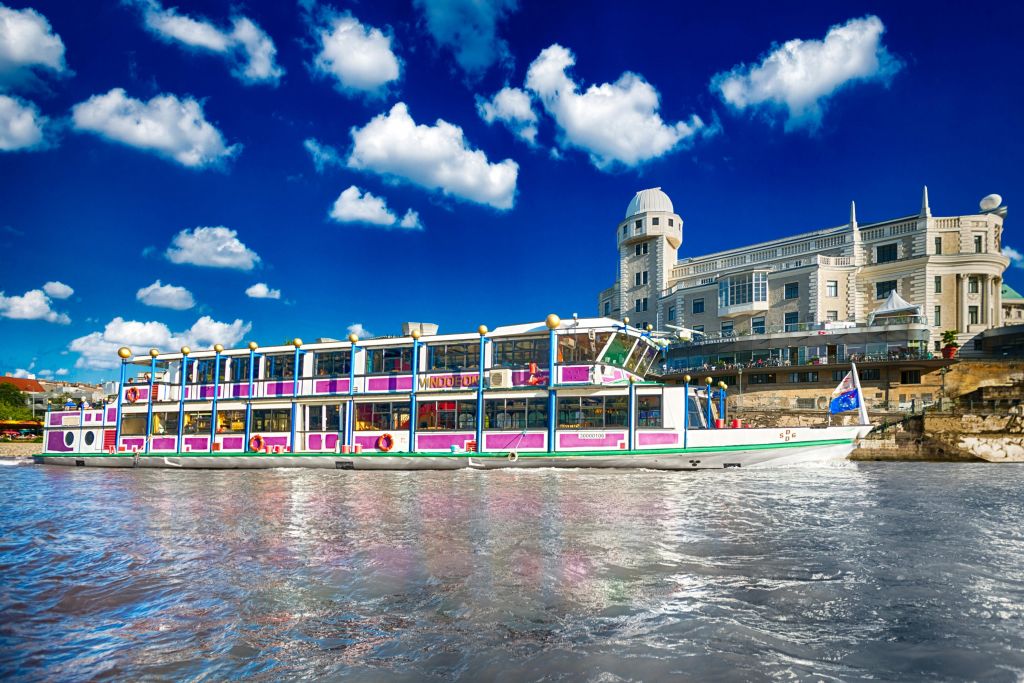 유서 깊은 건물과 구름이 가득한 밝고 푸른 하늘을 배경으로 화창한 날에 여러 개의 창문이 있는 다채로운 리버보트.