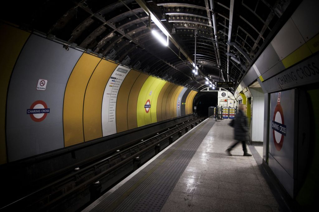 노란색과 흰색 벽, 머리 위 조명, 플랫폼을 걷는 한 사람이 있는 텅 빈 지하 열차 플랫폼입니다.