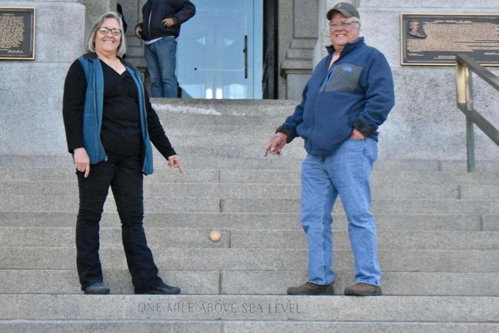 파란색 재킷과 청바지를 입은 사람이 플라크와 난간 근처 계단에 서 있습니다. 계단에 "해발 1마일" 이라고 새겨져 있습니다.