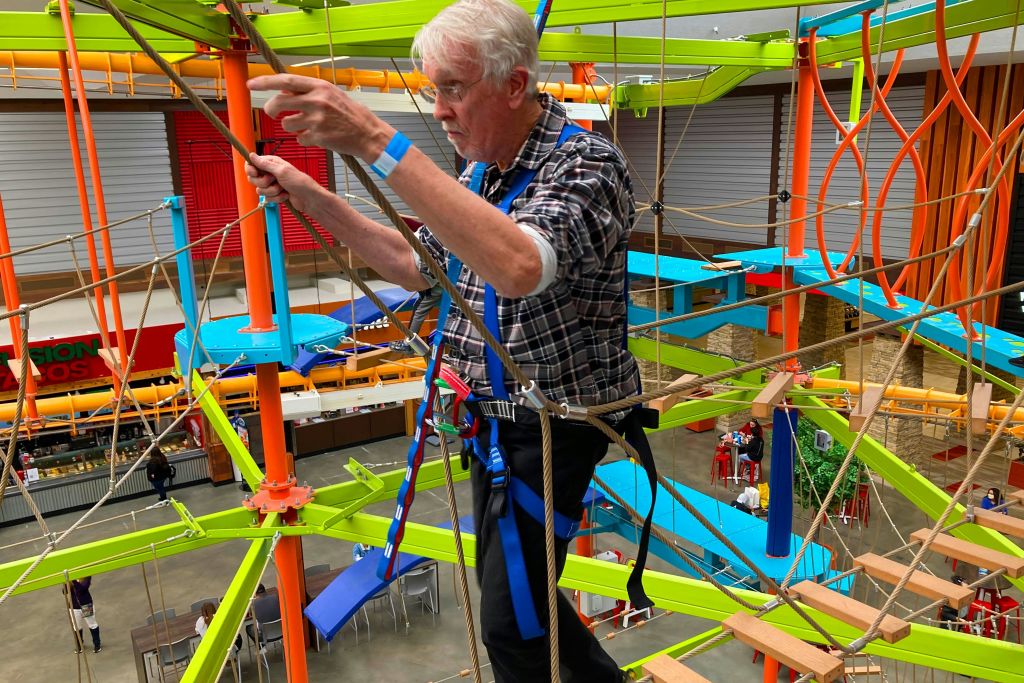 다채로운 색상의 실내 로프 코스를 항해하는 한 노인이 안전 하네스를 착용하고 걸음에 집중하고 있습니다.