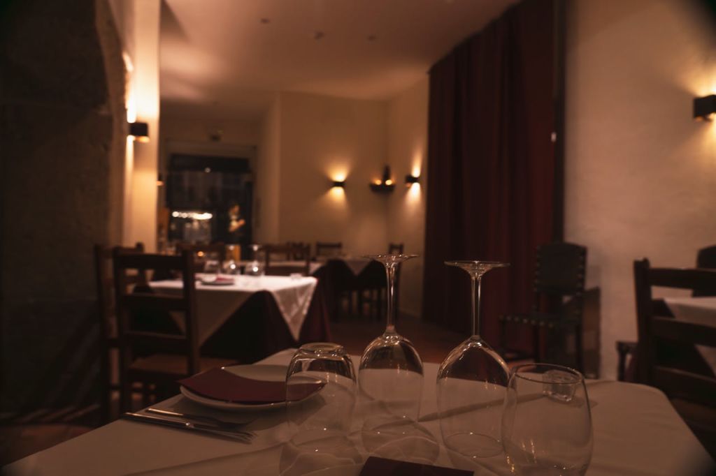 빈 테이블, 흰색 식탁보, 와인잔, 우아한 분위기가 있는 조명이 희미한 레스토랑입니다.