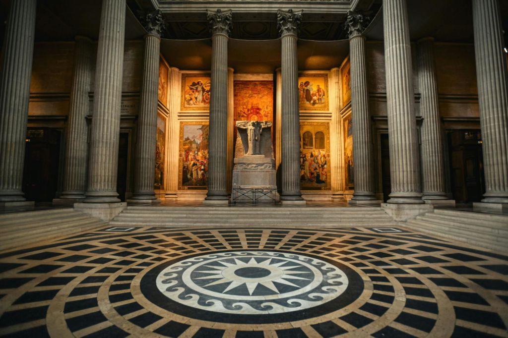 화려한 기둥, 정교한 바닥 모자이크, 중앙 동상을 둘러싼 조명 벽화가 있는 그랜드 홀입니다.