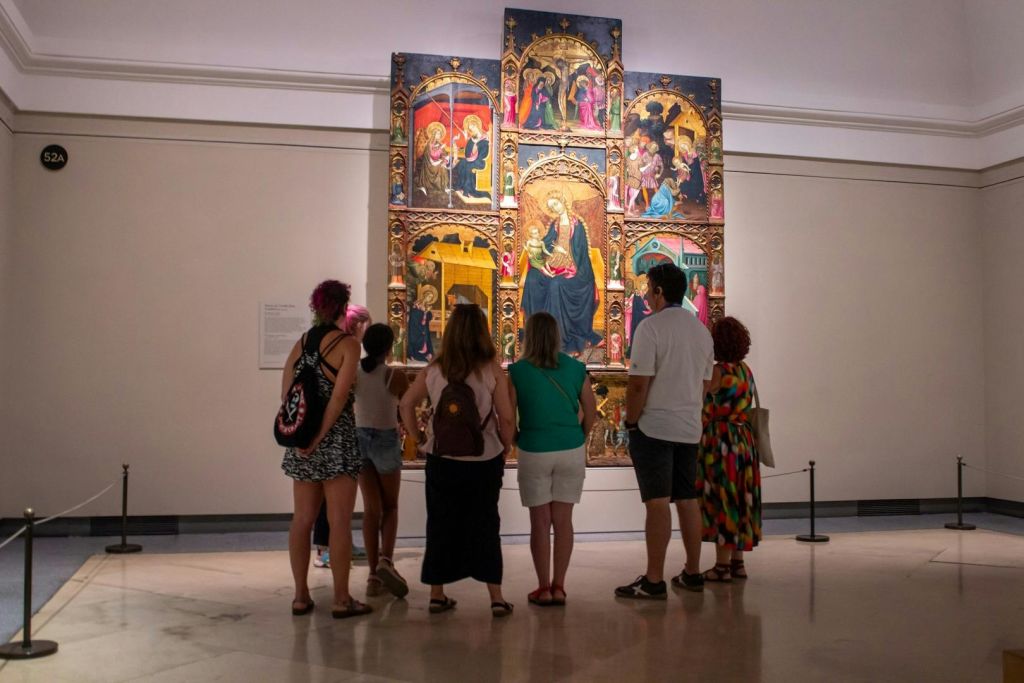 박물관 갤러리의 크고 디테일한 중세 제단 앞에 한 무리의 사람들이 서 있습니다.