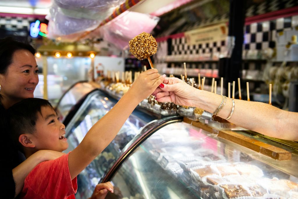 다양한 간식이 가득한 아이스크림 카운터 뒤에서 미소 짓는 소년과 여성이 카라멜 사과를 받습니다.
