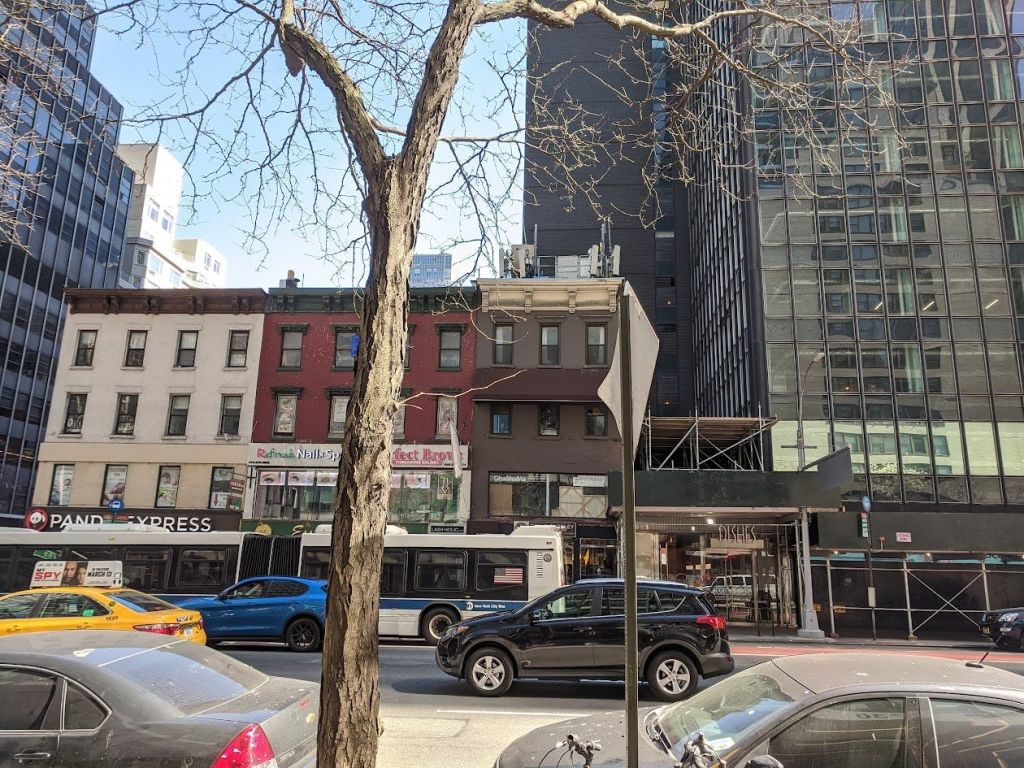 주차된 차와 버스, 다양한 스타일의 건물이 있는 시내 거리. 맨몸 나무 몸통과 표지판이 앞쪽에 있습니다.