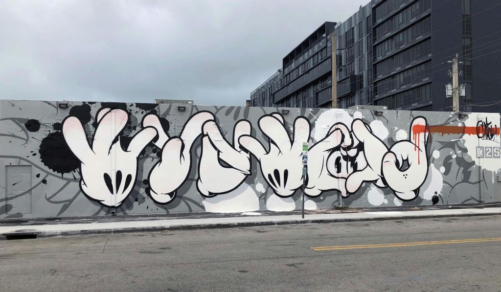 회색 건물이 배경으로 다양한 위치에 있는 일련의 양식화된 만화 같은 손을 묘사한 벽에 그라피티가 있습니다.