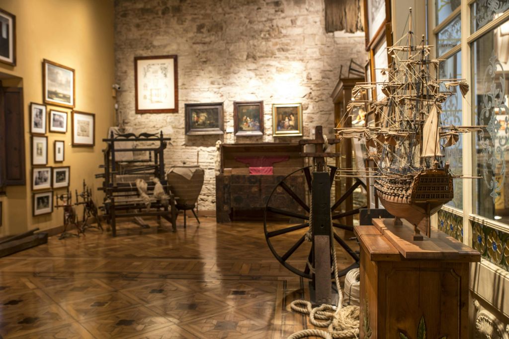 나무 바닥, 선박 모형, 빈티지 가구, 해양 유물, 돌 벽에 액자 그림이 있는 박물관 방.