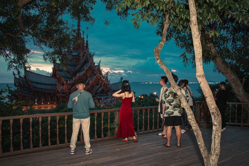 나무 데크에 앉아 있는 사람들은 저 멀리 황혼빛 하늘 아래 나무로 둘러싸인 화려한 사원을 감상합니다.