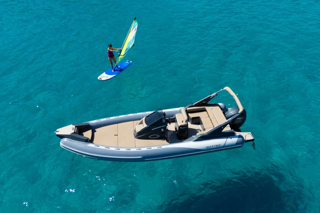 한 사람이 근처에서 윈드서핑을 하며 맑고 푸른 물 위에 있는 풍선 모터보트.