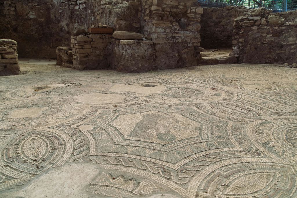 기하학적 모양과 중앙에 동물 형상이 있는 복잡한 모자이크 바닥이 있는 고대 석조 유적.