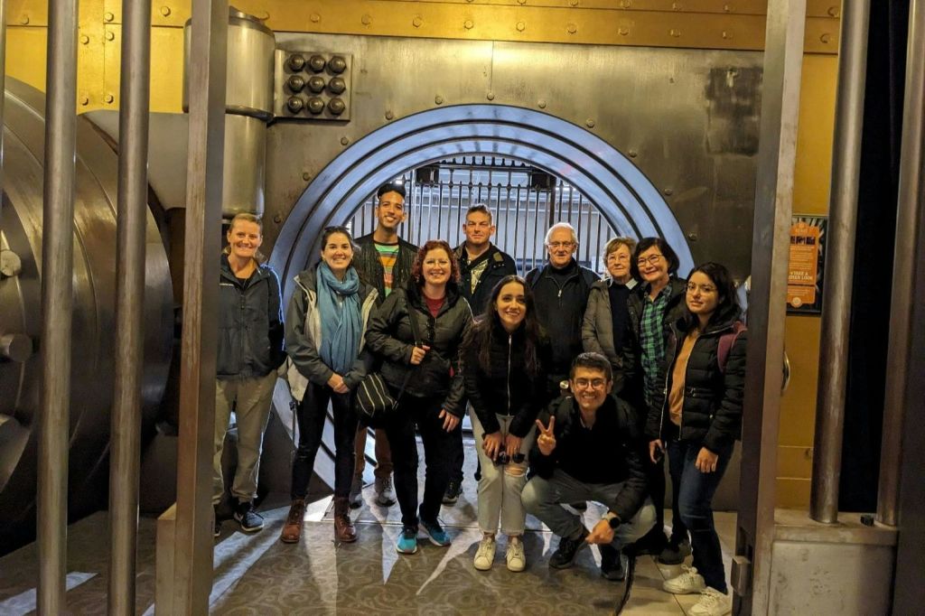 내부에서 크고 둥근 금속 금고 문 앞에서 포즈를 취하고 있는 한 무리의 사람들.