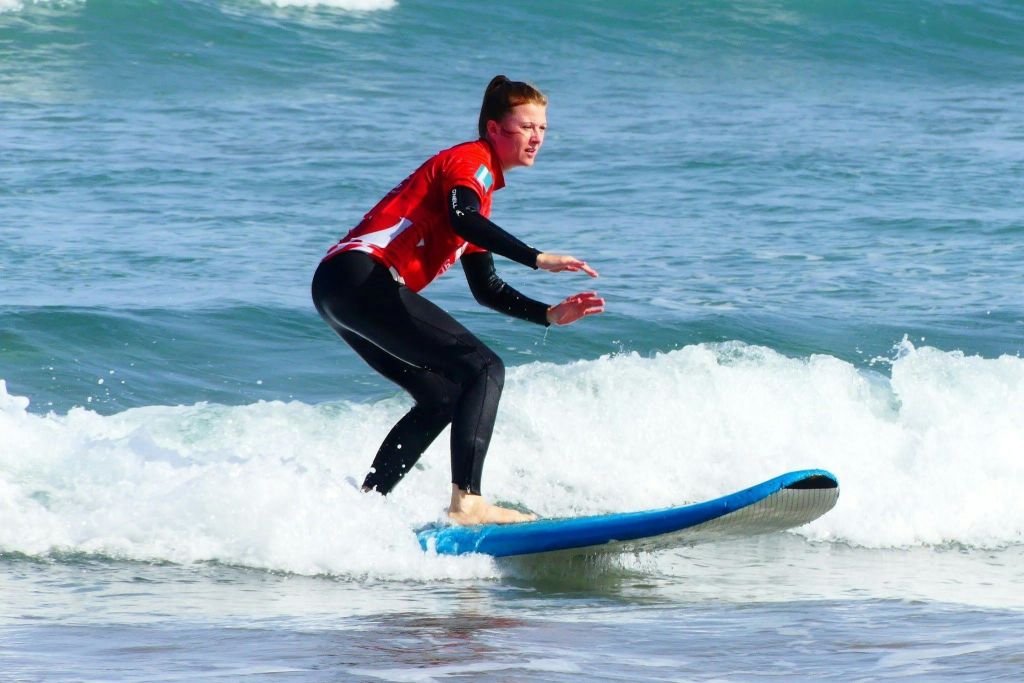 바다 파도 속에서 파란색 서핑 보드를 타고 서핑하는 빨간색 셔츠와 검은색 잠수복을 입은 사람.