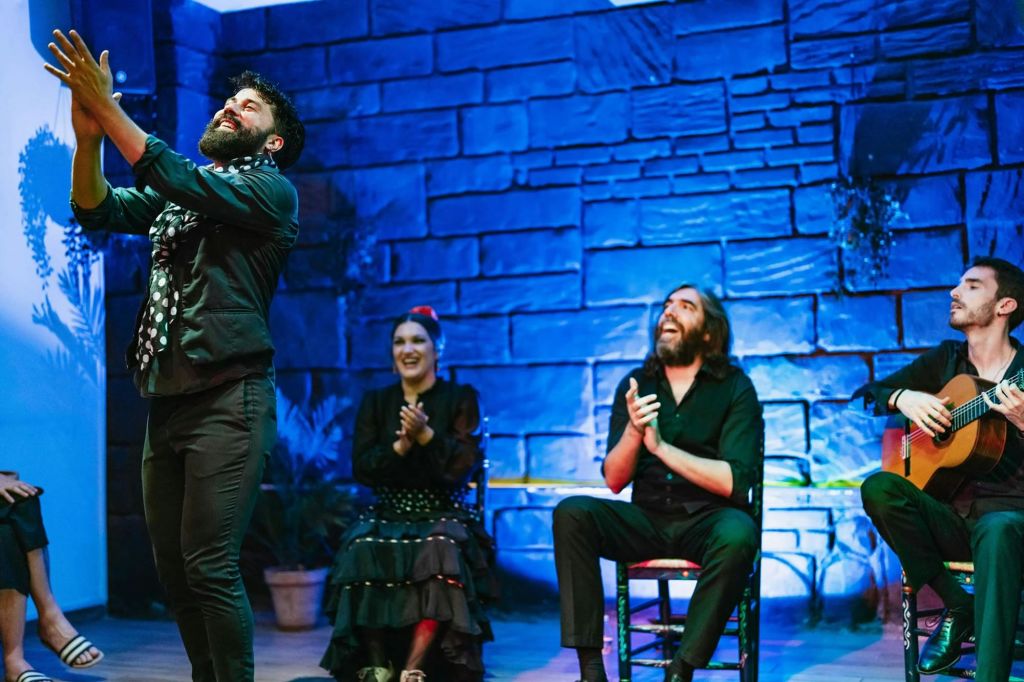 플라멩코 복장을 한 남성이 열정적으로 박수를 치고, 자리에 앉은 두 사람이 플라멩코 의상을 입고 미소를 지으며 박수를 치고 있습니다.