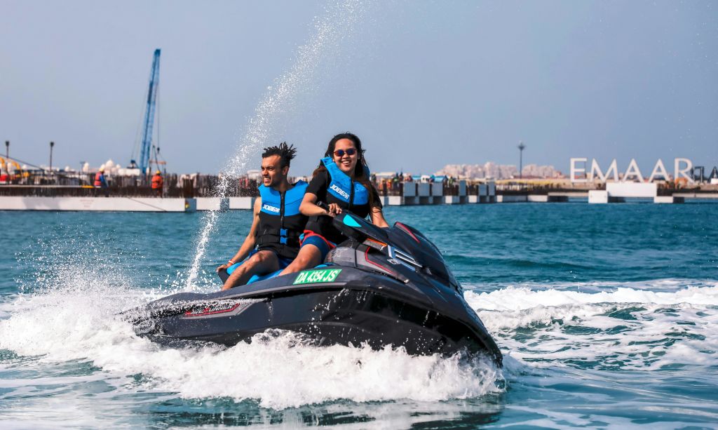 구명조끼를 입은 두 사람이 부두와 크레인을 배경으로 물 위에서 제트 스키를 타고 있습니다.