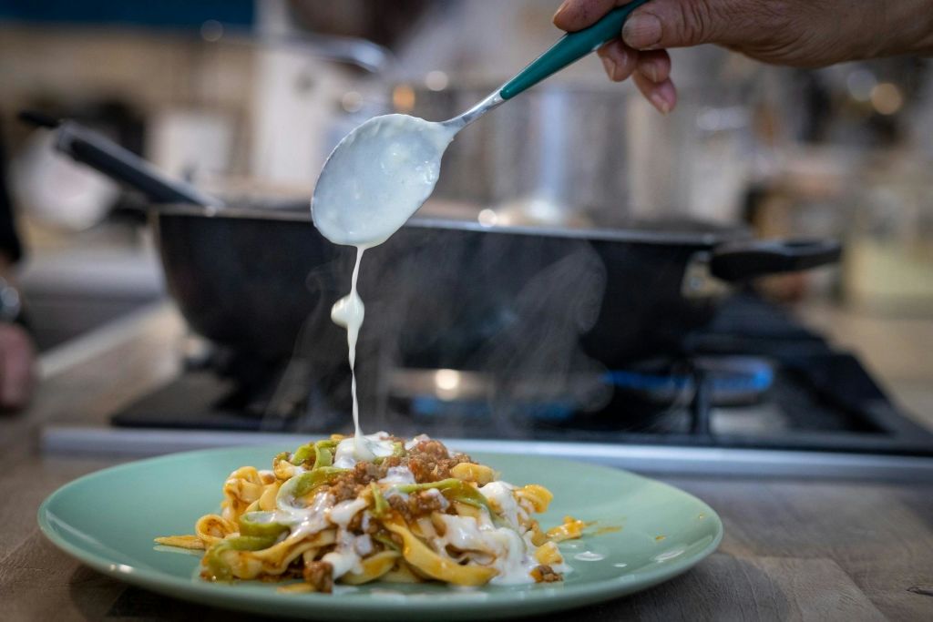 주방에서 녹색 접시에 야채와 고기가 담긴 찐 파스타 위에 크리미한 소스를 손으로 붓습니다.