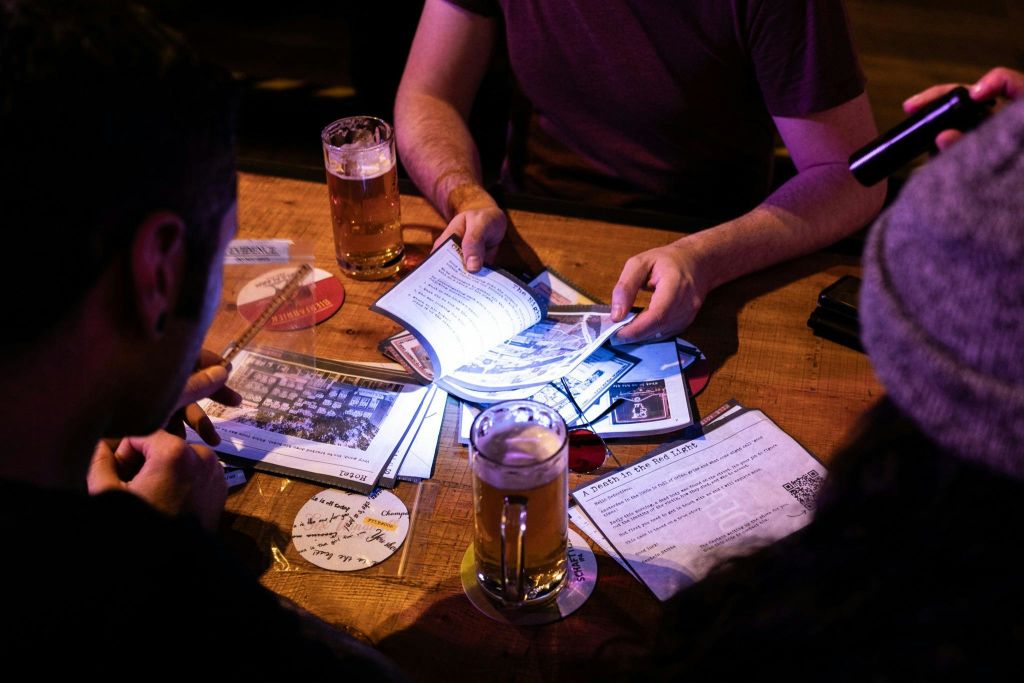 여러 사람이 서류와 맥주잔이 놓인 나무 테이블에 앉아 논문을 교환하고 토론하고 있습니다.