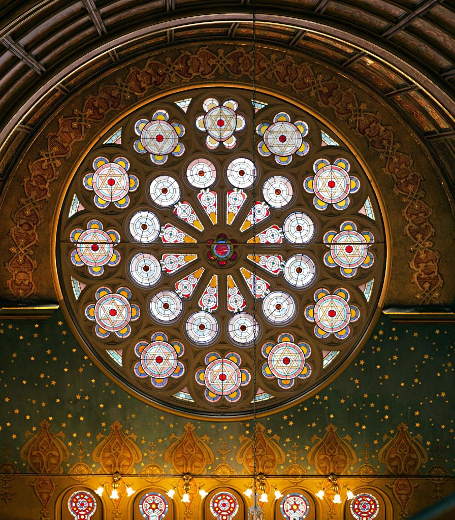 화려하게 장식된 벽에 장식된 원형 스테인드글라스 창으로, 정교한 꽃 무늬와 선명한 색상이 특징입니다.