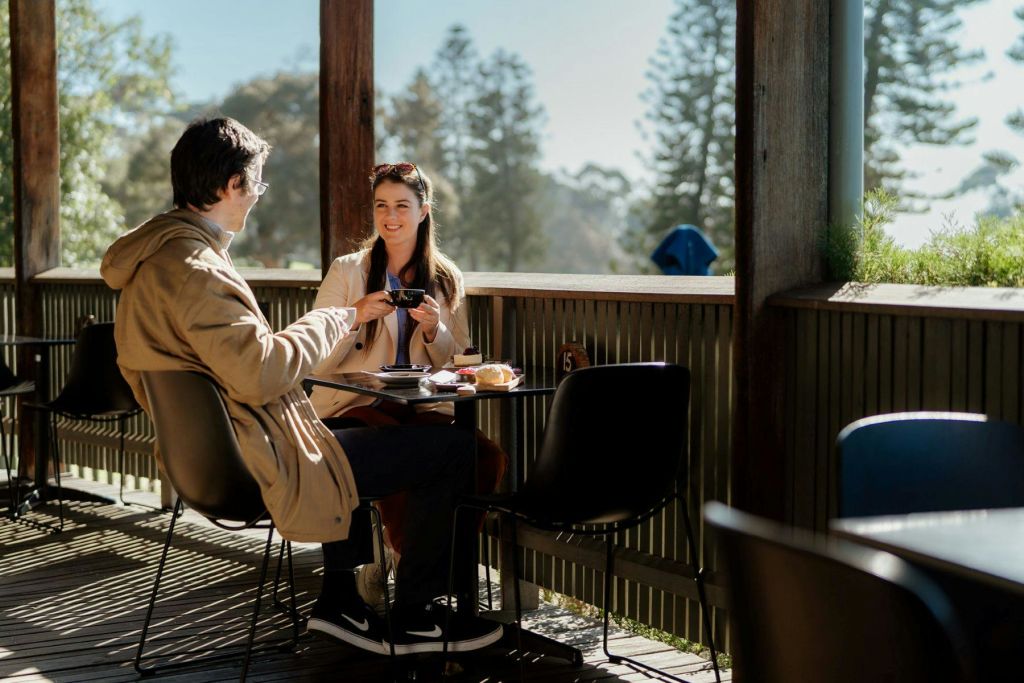 나무를 배경으로 햇살이 내리쬐는 날 야외 카페에서 커피와 페이스트리를 즐기는 두 사람.