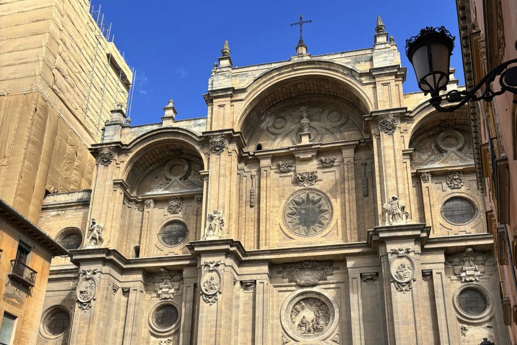 아치, 세부 조각, 둥근 창문, 맑고 푸른 하늘 아래 십자가가 있는 역사적인 건물의 화려한 외관.