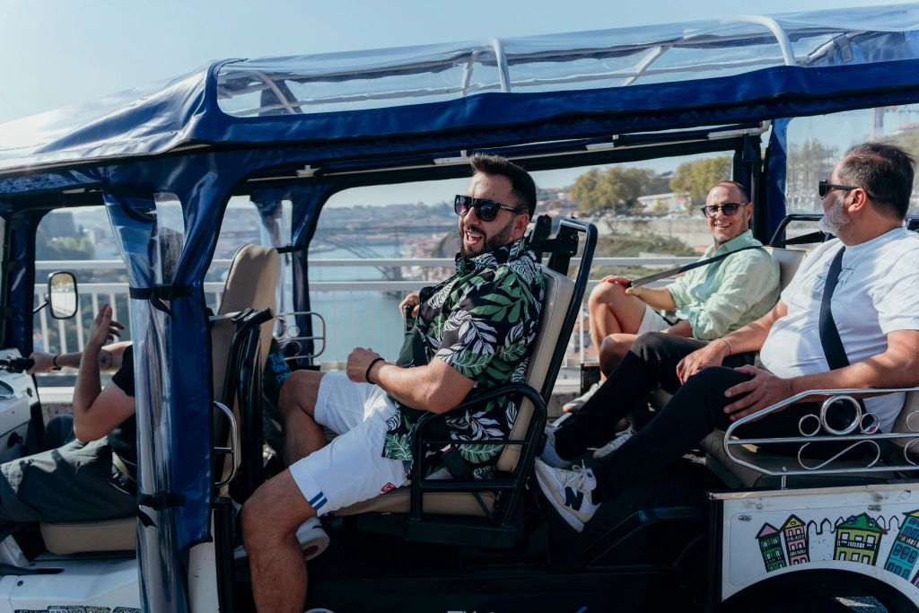 강과 도시 건물의 경치 좋은 배경을 가진 개방형 차량 안에 세 명의 남성이 앉아 있습니다.