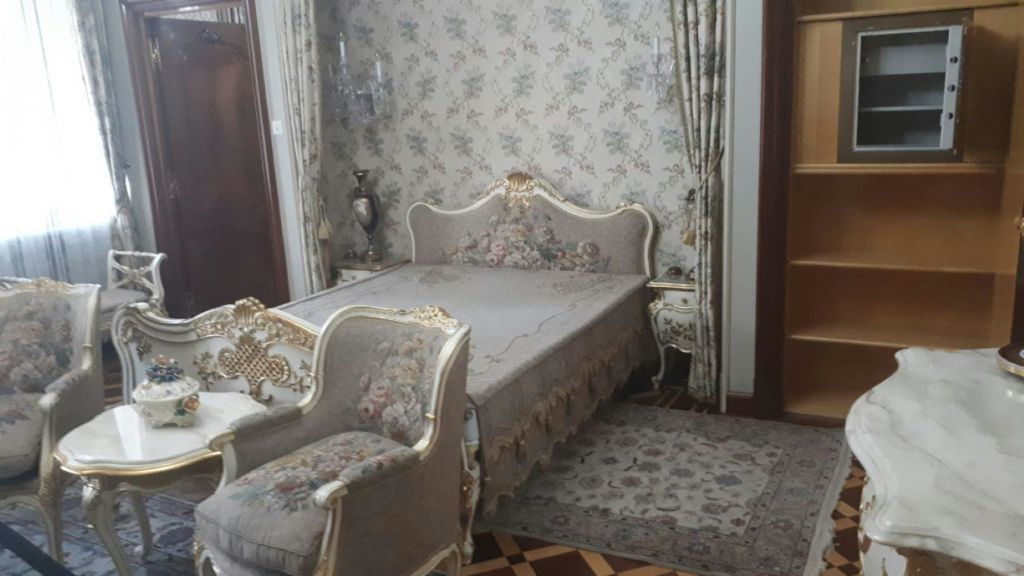 꽃무늬 벽지가 있는 화려한 침실, 꽃무늬 실내 장식이 있는 조각된 침대, 어울리는 안락의자, 사이드 테이블, 무늬 러그.