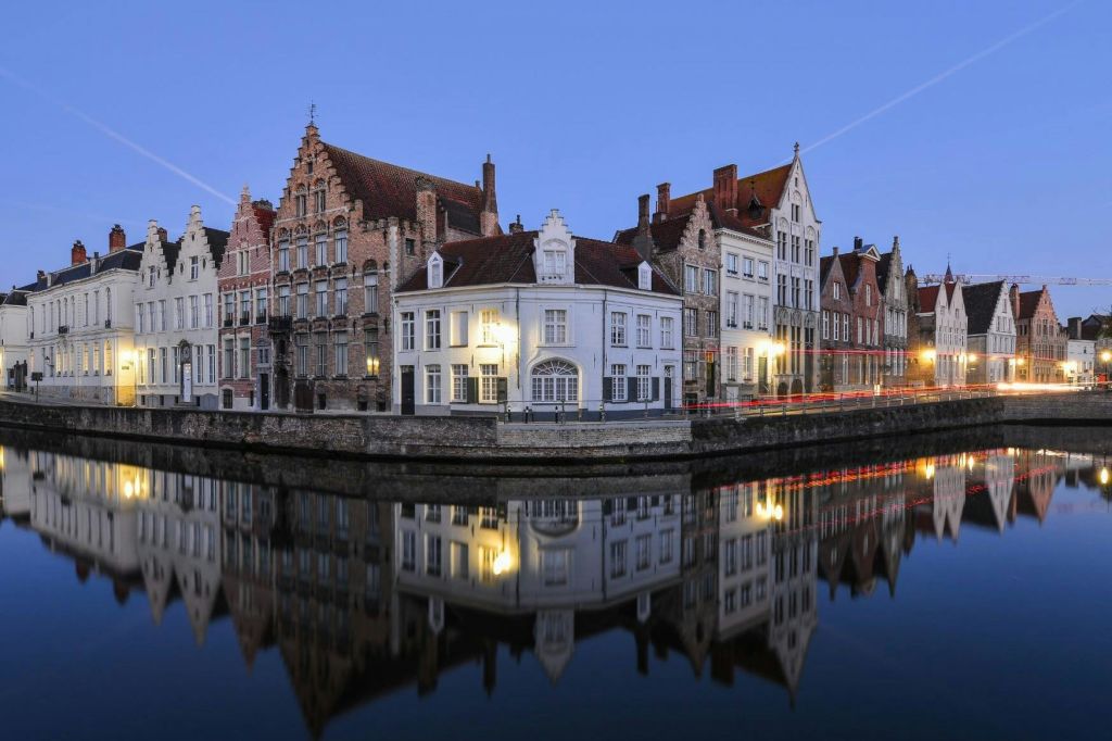 황혼 하늘 아래 잔잔한 물에 반사된 화려한 외관과 화려한 지붕을 갖춘 운하 쪽 유럽 건물.