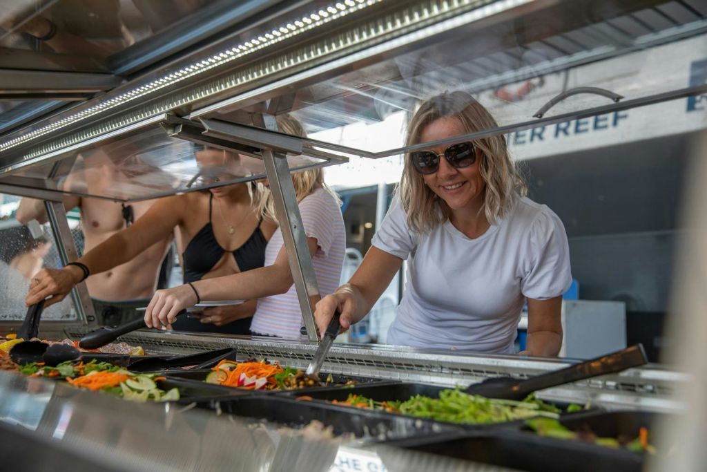 샐러드 바에서 선글라스를 쓴 미소를 짓는 여성이 트레이에 다양한 신선한 야채가 보입니다.