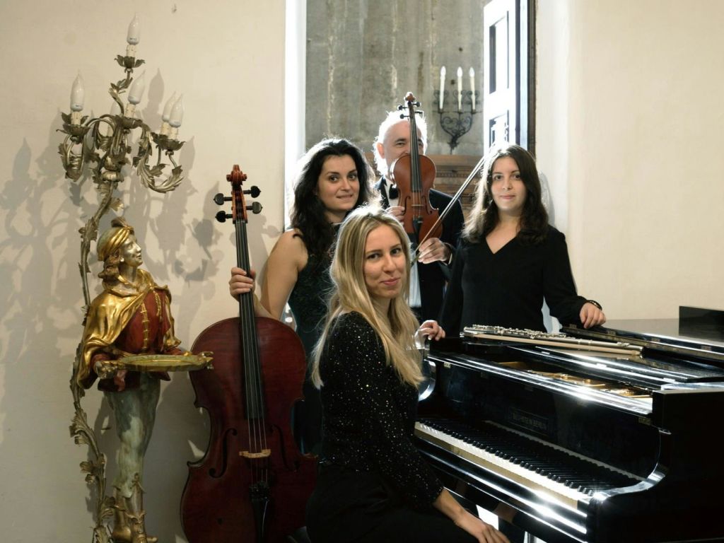 칸델라브라와 나무 장식이 있는 방에서 현악기와 피아노 포즈를 취하는 네 명의 뮤지션.