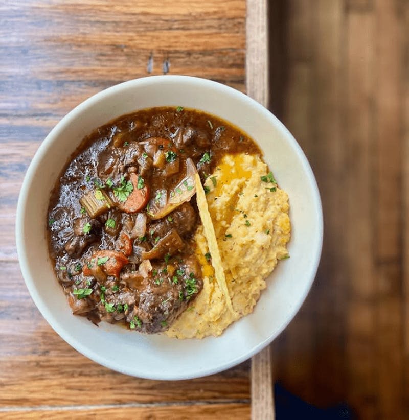 나무 테이블 위에 야채와 폴렌타를 올린 쇠고기 스튜 한 그릇.